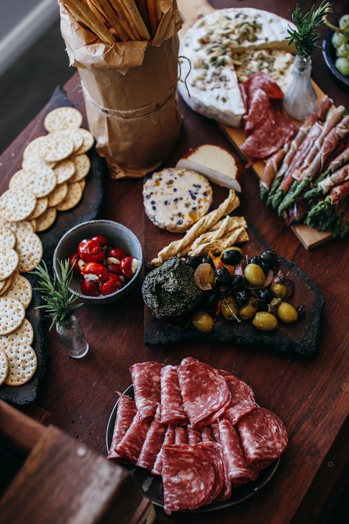 From above of assorted delicious cold cuts with olives and crackers served on wooden table with creamy cheese and dried tomatoes